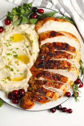 A sliced air fryer turkey breast on a plate with mashed potatoes, cranberries and herbs.