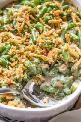 a cooked green bean casserole recipe in a white serving dish with a spoon