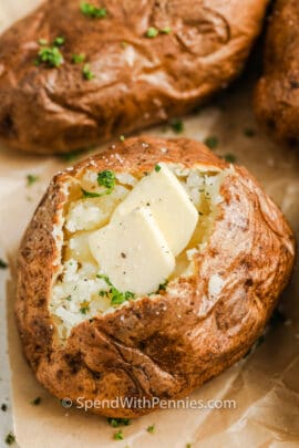 close up of Air Fryer Baked Potatoes cut open with butter and seasoning