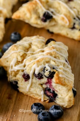 a blueberry scone with drizzle on a wood cutting board