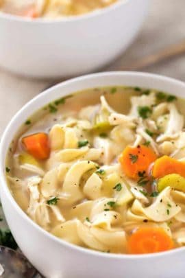 White bowl of chicken noodle soup with carrots