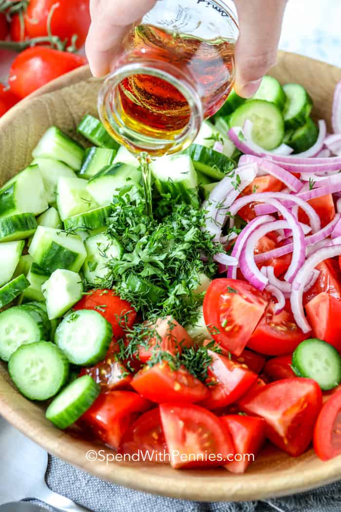 Pouring dressing over Cucumber Tomato Salad in a wooden bowl