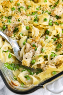 Serving chicken noodle casserole from a baking dish with a silver serving spoon