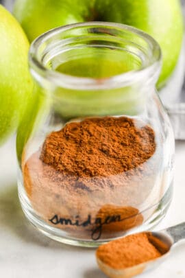 close up of Apple Pie Spice in a glass jar with apples in the back