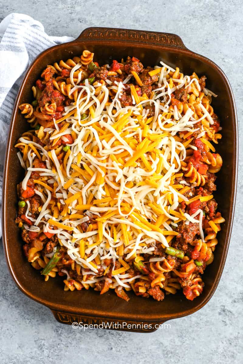cheese on top of sauce, noodles and vegetables in a casserole dish for hamburger casserole