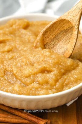 a bowl of homemade applesauce being stirred with a wooden spoon