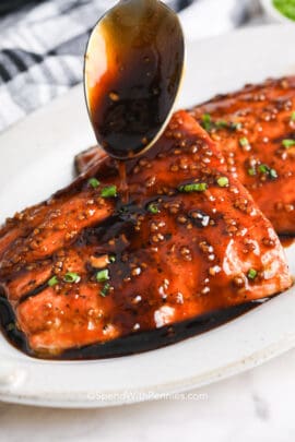 spooning sauce over two honey glazed salmon filets with chives