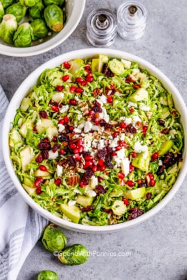 Brussels sprout salad in a white bowl topped with feta and pomegranate