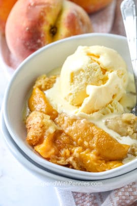 Peach Dump Cake in a white bowl with vanilla ice cream