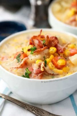 Corn chowder in a bowl topped with corn, bacon and parsley with a spoon