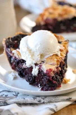 Slice of Blueberry Pie on a white plate with ice cream on top