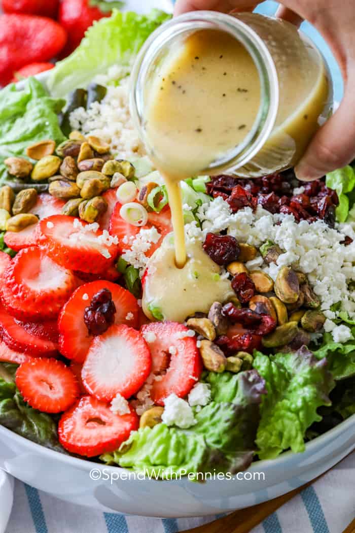 Strawberry pistachio salad in a bowl with dressing being poured on