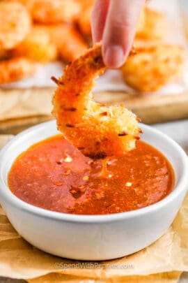 A breaded shrimp being dipped in a bowl of sweet chili sauce