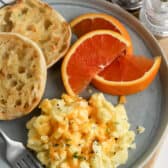 scrambled eggs on a plate with english muffins and orange wedges