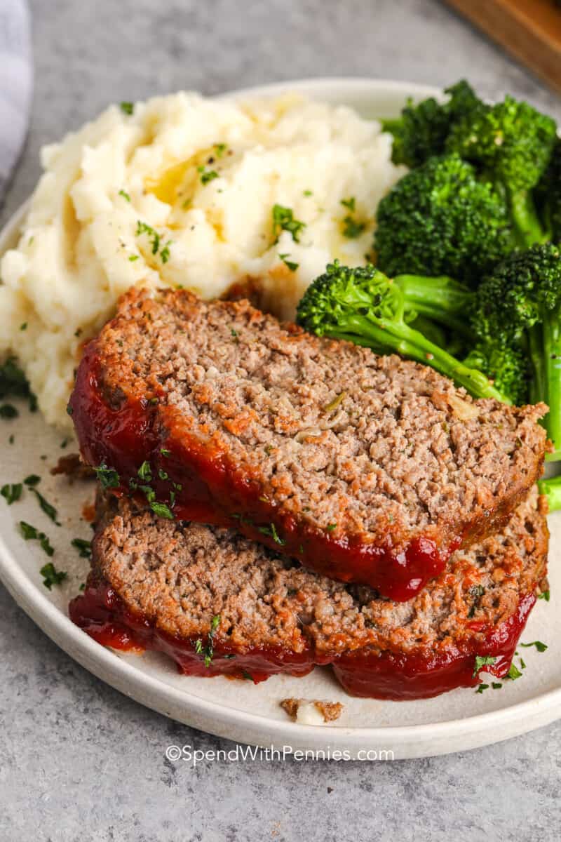 2 slices of homemade meatloaf on a plate with mashed potatoes and broccoli