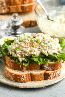 close up of a Tuna Egg Salad sandwich on a plate with bowl full of salad in the back